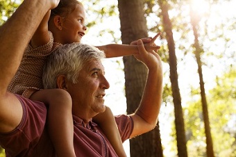 young girl sitting on grandpa's shoulders outdoors